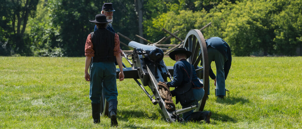 Union soldiers preparing a cannon for firing, working together as they load ammunition and adjust the cannon's position. Dressed in blue uniforms, their expressions are focused and determined, highlighting the teamwork and urgency involved in artillery preparation during the Civil War.